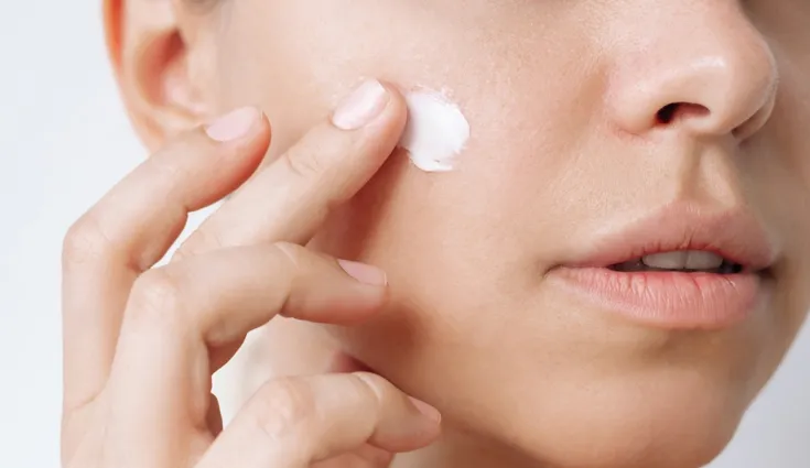 Close up of a young woman applying moisturizer to her skin. 