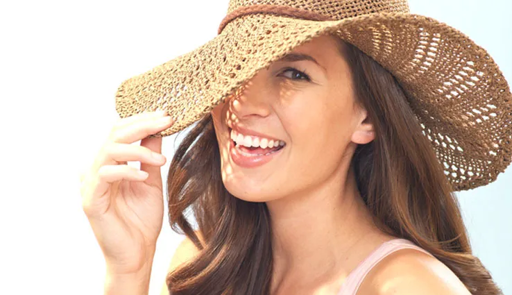 Woman smiling while shading face with a sun hat. 