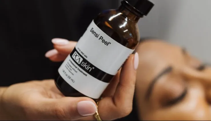A bottle of PCA SKIN Sensi Peel being held in front of someone currently getting the peel treatment.