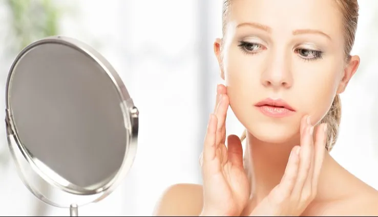 A woman looking concerned at her skin for acne in a mirror.
