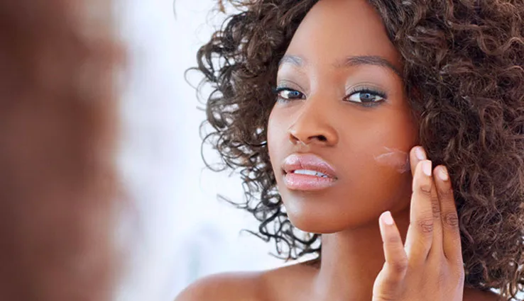 African American woman applying moisturizer to her face.