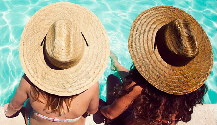 Two young women in hats sitting beside the pool.