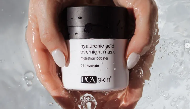 A jar of PCA SKIN Hyaluronic Acid Overnight Mask being held right above clear water.
