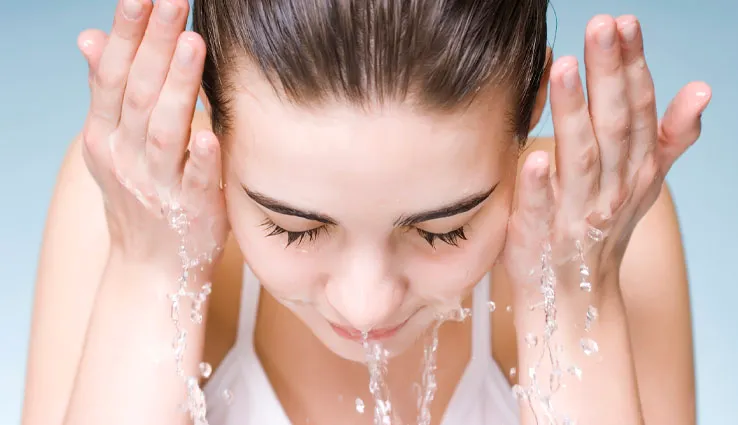 A woman washing her face with water splashing around her hands.