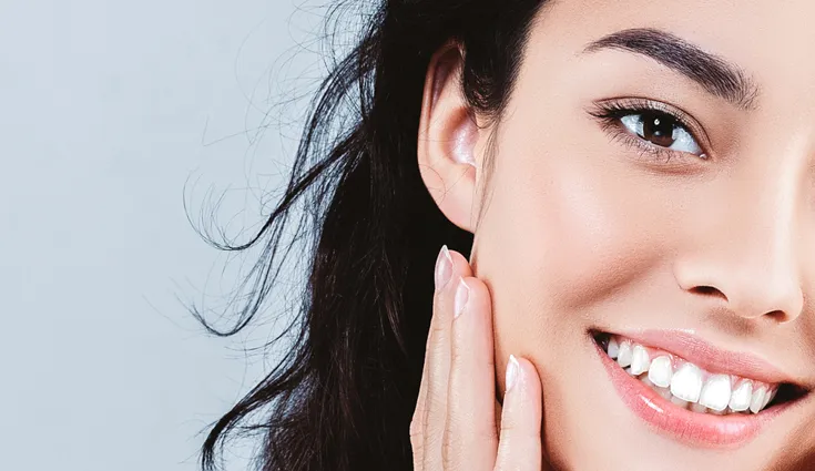  A smiling woman with clear skin touches either side of her face.