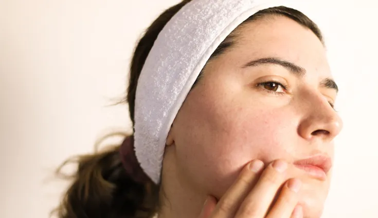 A woman examines the irritated skin on her face. 